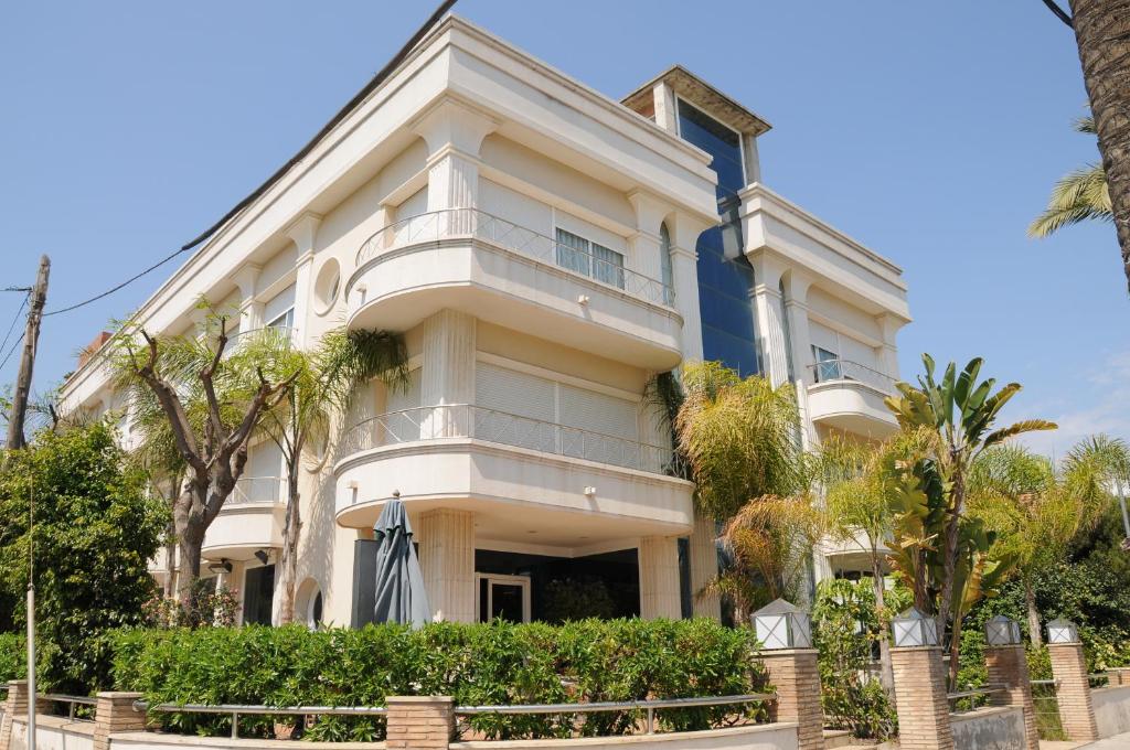 un grand bâtiment blanc avec des arbres devant lui dans l'établissement MAREA ApartHotel, à Vilanova i la Geltrú