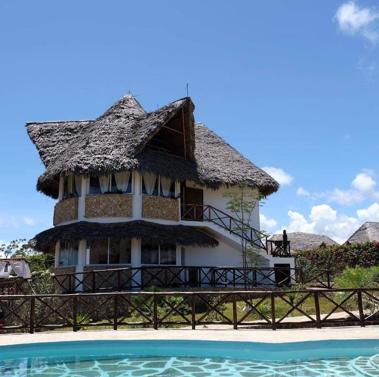 a house with a thatched roof next to a swimming pool at Miky House in Watamu