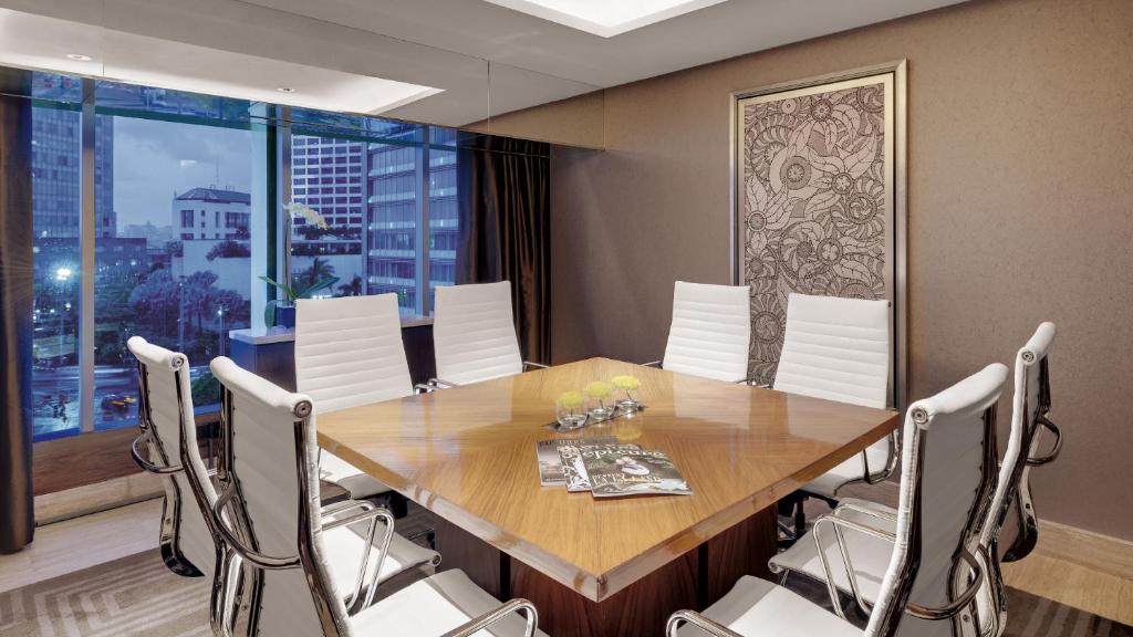 a dining room with a wooden table and white chairs at Hotel Indonesia Kempinski Jakarta in Jakarta