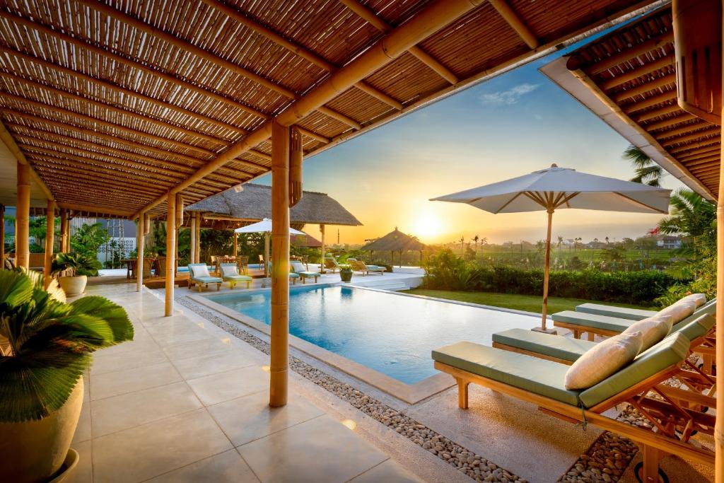 una piscina al aire libre con tumbonas y sombrilla en Bloomfield Umalas, en Canggu