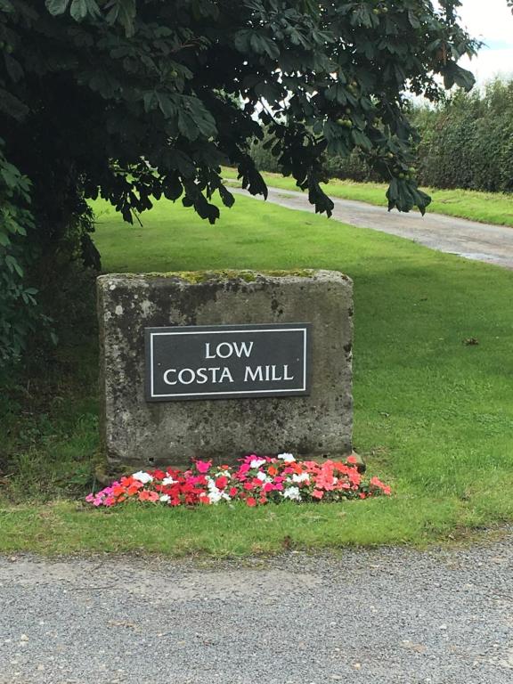 a sign for low costa mill in a park with flowers at Low Costa Mill in Pickering