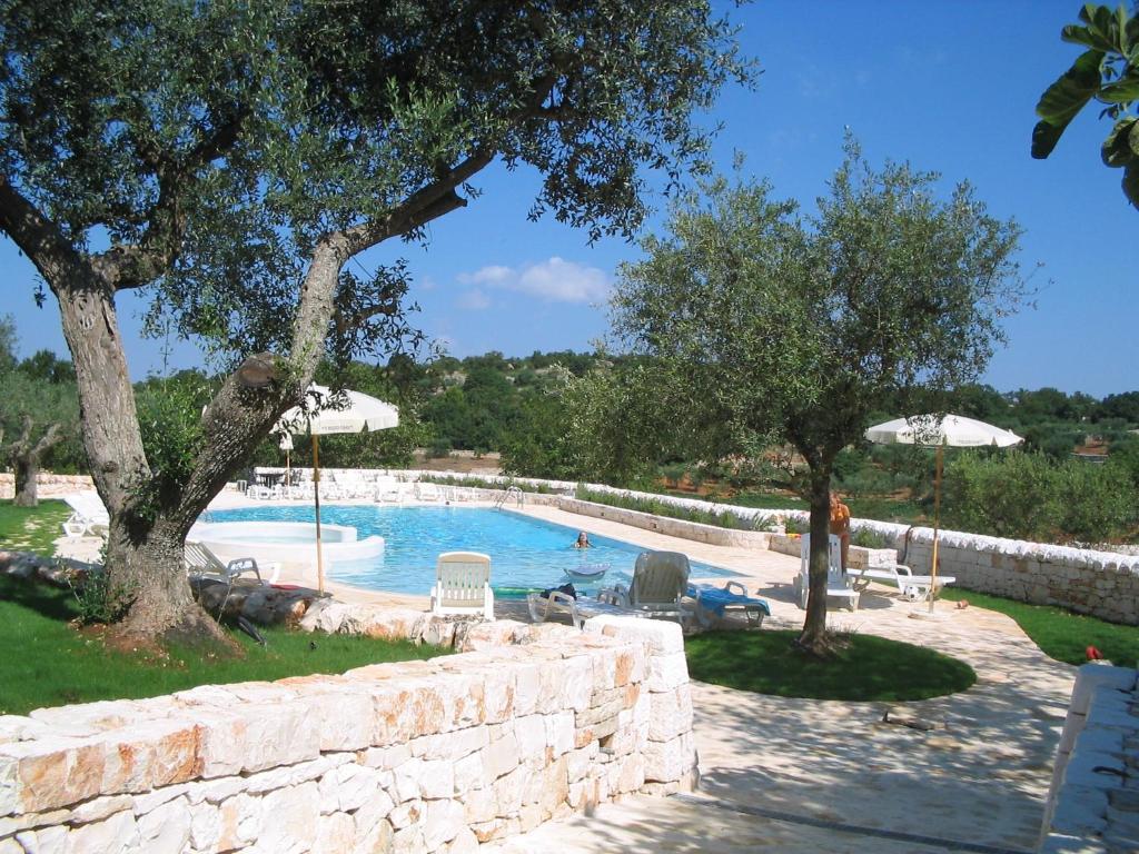 a swimming pool with chairs and umbrellas and trees at Truddhi Casa e Cucina di Puglia in Locorotondo