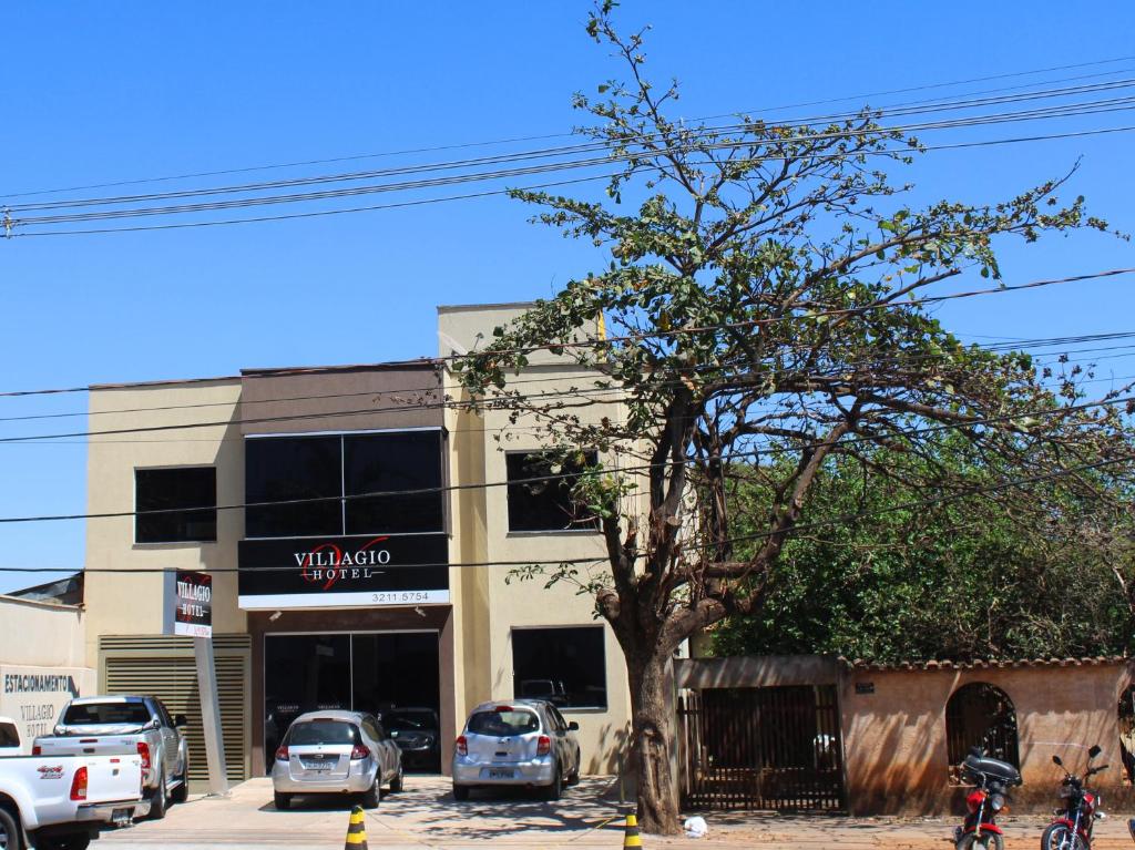 a tree in front of a building with parked cars at Luz Hotel in Goiânia