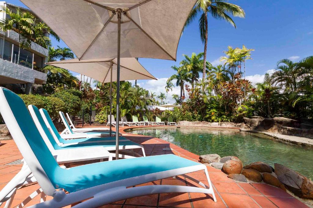 een groep stoelen en een parasol naast een zwembad bij Club Tropical Resort with Onsite Reception & Check In in Port Douglas