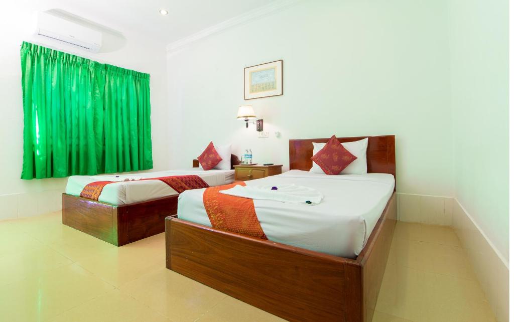 two beds in a room with green curtains at Blossoming Romduol Boutique in Siem Reap