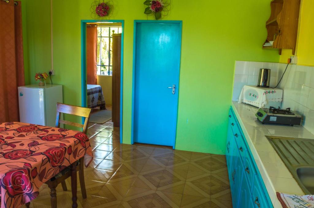 a kitchen with a blue door and a table and a refrigerator at Merlin Guest House in Rodrigues Island