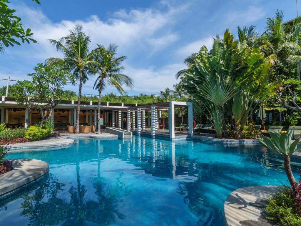 Kokonut Suites Seminyak في سمينياك: مسبح بالنخيل ومبنى