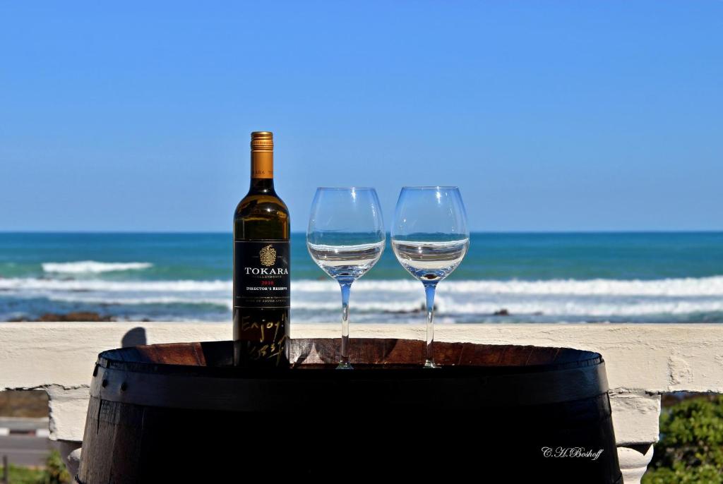 a bottle of wine and two wine glasses on a barrel on the beach at Walkerbay Accommodation in Gansbaai