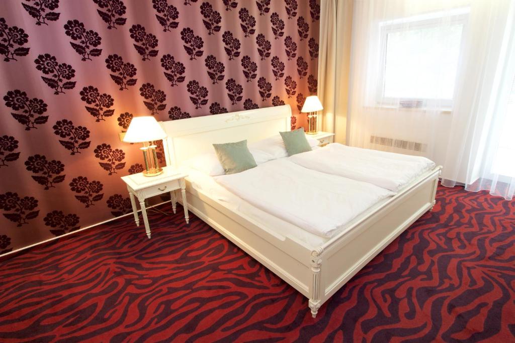 a bedroom with a white bed and a red carpet at Hotel Galant Lednice in Lednice