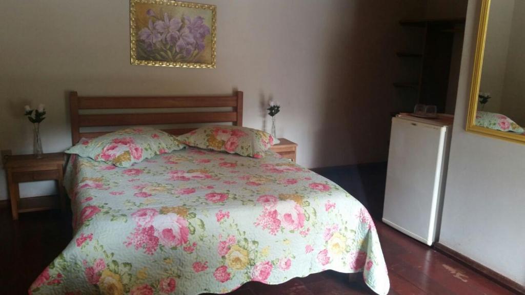 1 dormitorio con 1 cama con colcha de flores y nevera en Pousada Nascer, en Visconde De Maua
