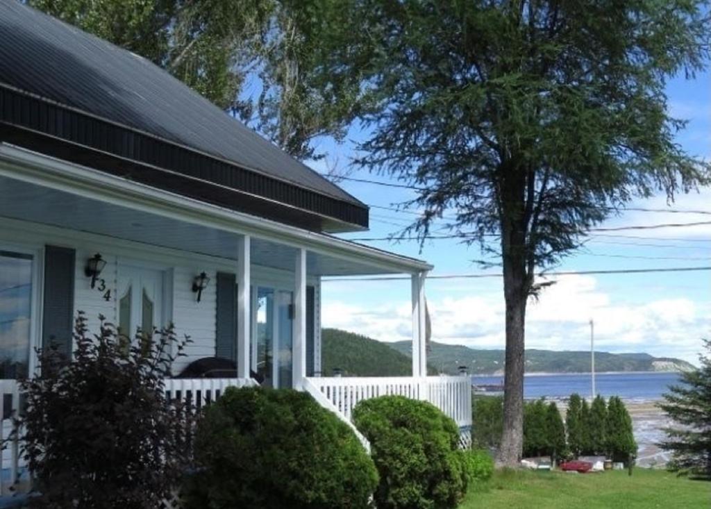 ein weißes Haus mit Blick auf das Wasser in der Unterkunft Gîte de la colline in Baie-Sainte-Catherine