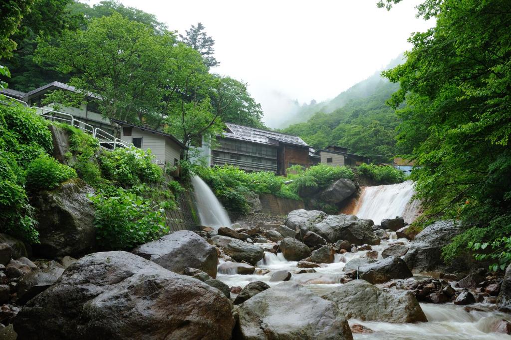 a river with rocks in front of a waterfall at Namegawaonsen Fukushimaya in Yonezawa
