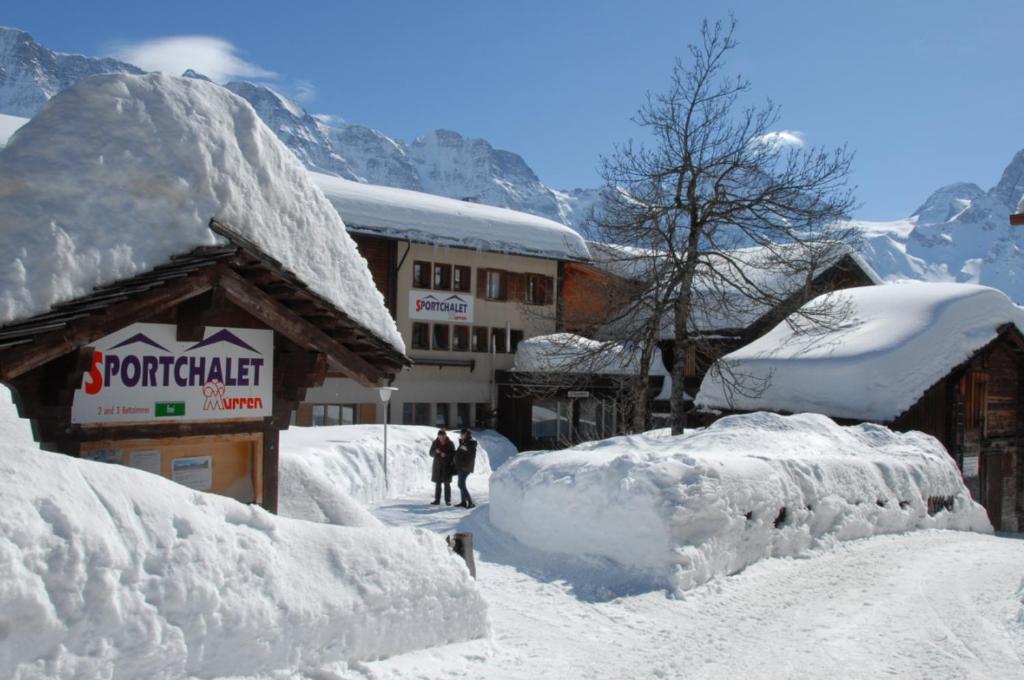 ミューレンにあるスポートシャレー ミューレンの雪に覆われた建物の前に立つ二人