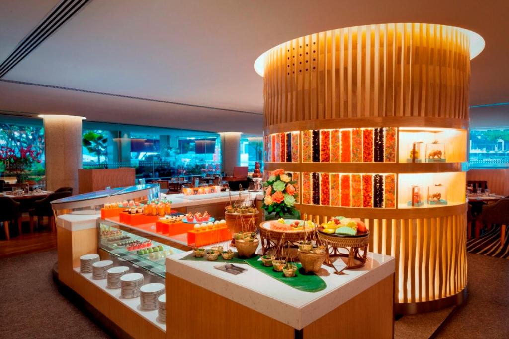 A brightly lit buffet counter with plated food, desserts, fruit and tableware.