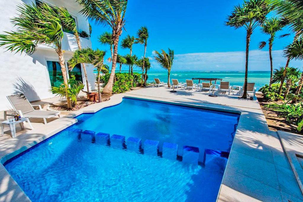 a swimming pool with palm trees and the ocean at Villa Mar Azul Luxury Villa in Tulum