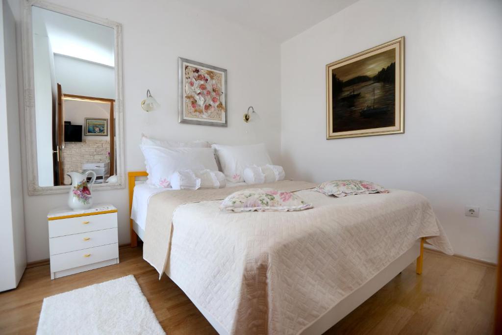 een witte slaapkamer met 2 bedden en een spiegel bij Apartmani Gloria in Brodarica