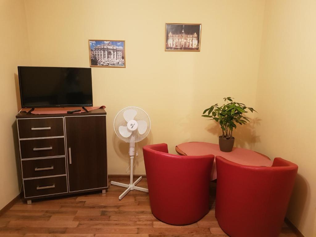 Habitación con 2 sillas rojas, mesa y TV. en Euro Zajazd - Casa Di Fulvio Maria Viola, en Bielsko-Biala