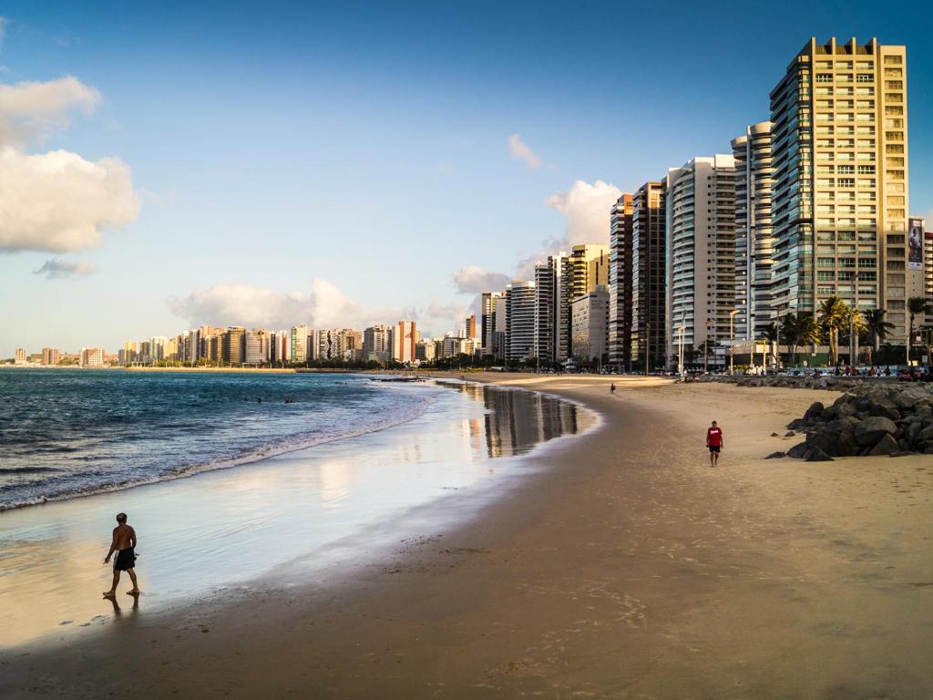 dos personas caminando en una playa con edificios altos en PORTO DE IRACEMA - FVP Group, en Fortaleza