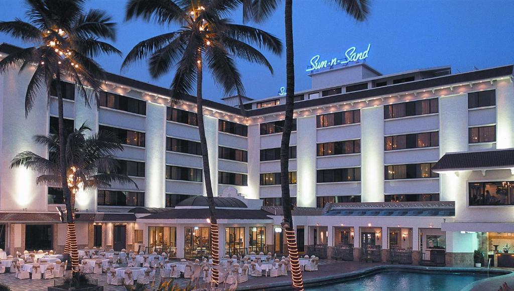a hotel with a pool and palm trees in front of it at Sun-n-Sand Mumbai Juhu Beach in Mumbai