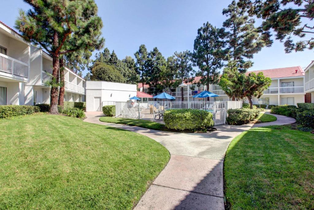 a walkway in front of a building with trees and grass at Motel 6-Santa Ana, CA - Irvine - Orange County Airport in Santa Ana