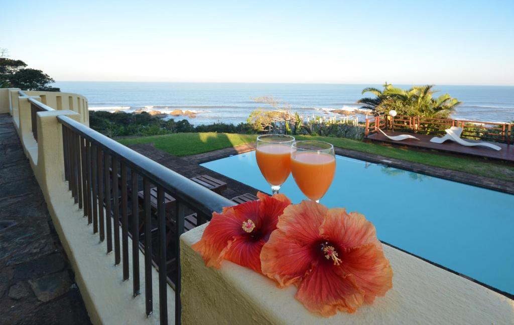 マーゲートにあるBeachcomber Bay Guest House In South Africaのバルコニーに飾られたオレンジと赤の花のグラス2杯