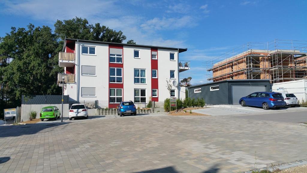 un edificio bianco e rosso con auto parcheggiate in un parcheggio di FeWo Brombachsee - Sonnentag West a Röttenbach