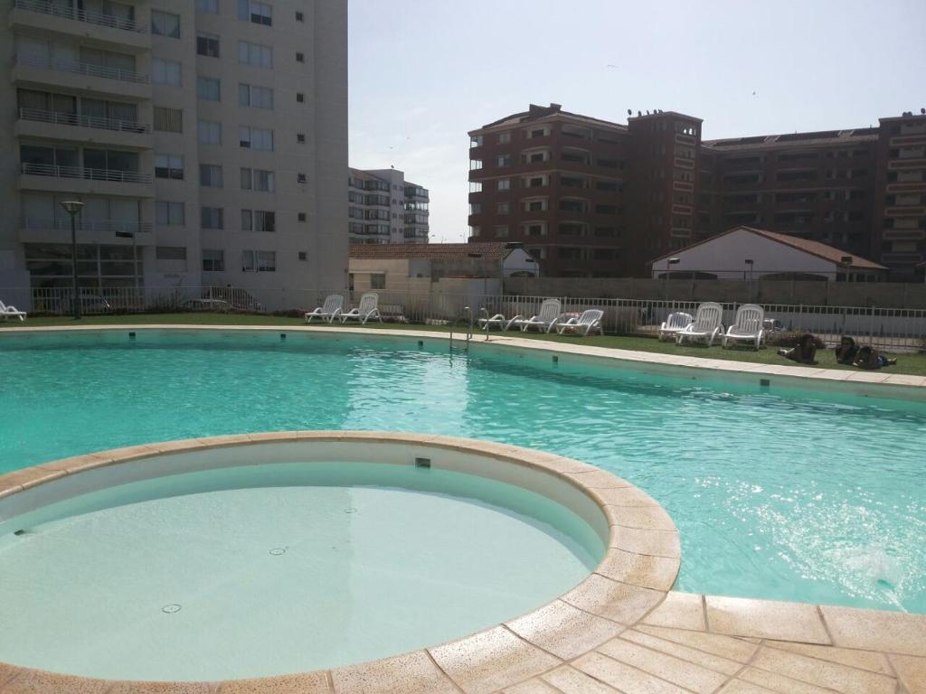 uma grande piscina de água azul com cadeiras e edifícios em Departamento Serena Pacífico em La Serena