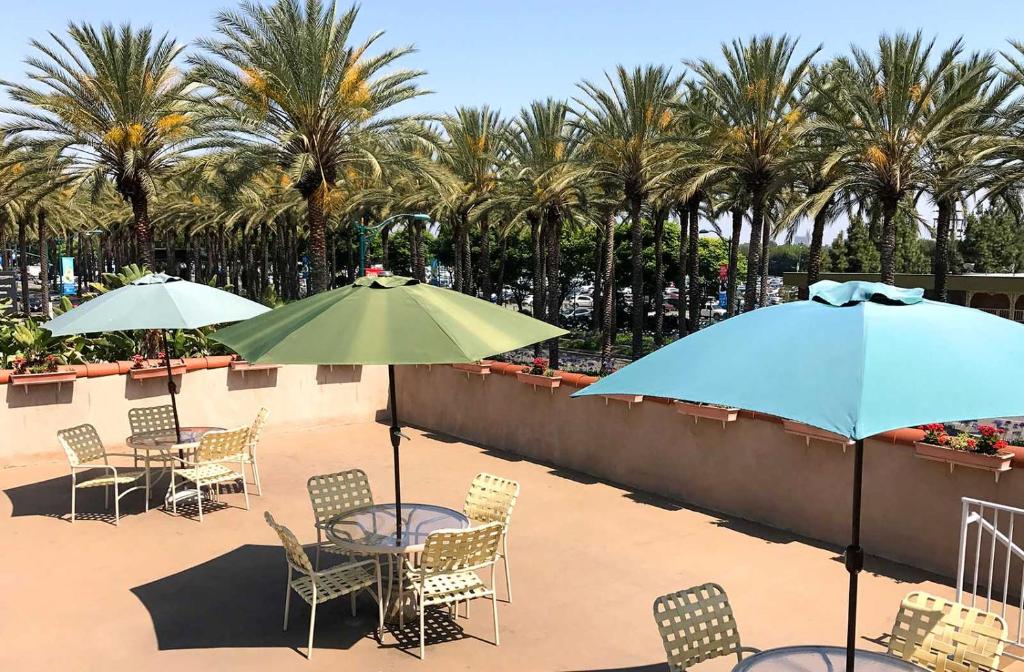 a patio with tables and chairs with umbrellas and palm trees at Kings Inn Anaheim at The Park & Convention Center in Anaheim