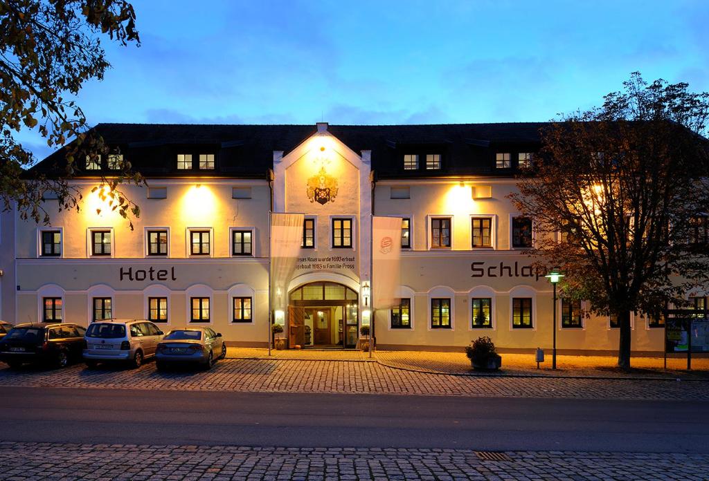 un grand bâtiment blanc avec des voitures garées devant lui dans l'établissement Landhotel Schlappinger-Hof, à Reisbach