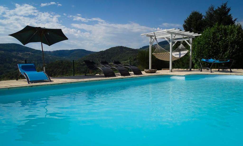 a blue swimming pool with chairs and an umbrella at Chambres d'Hôtes Le Crouzat in Empurany