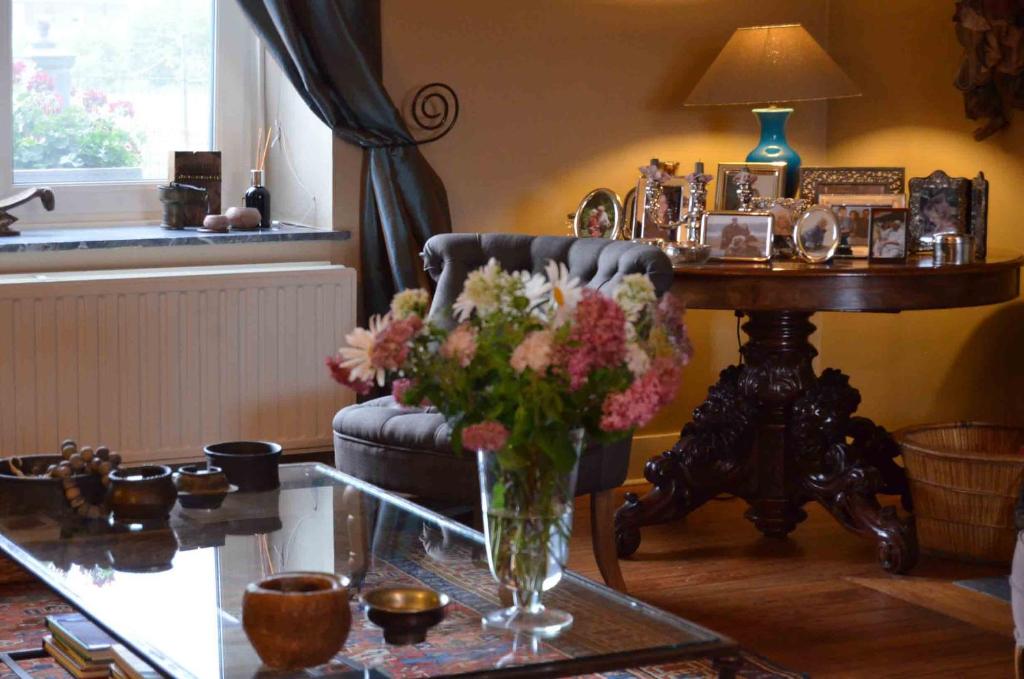 uma sala de estar com uma cadeira e uma mesa com um vaso de flores em Les Glaneuses em Mettet