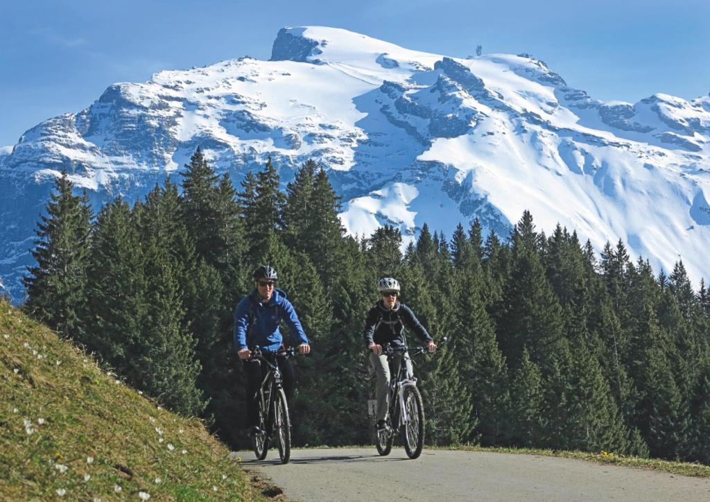 two people riding bikes down a road with a snow covered mountain at Hotel Engelberg "mein Trail Hotel" in Engelberg