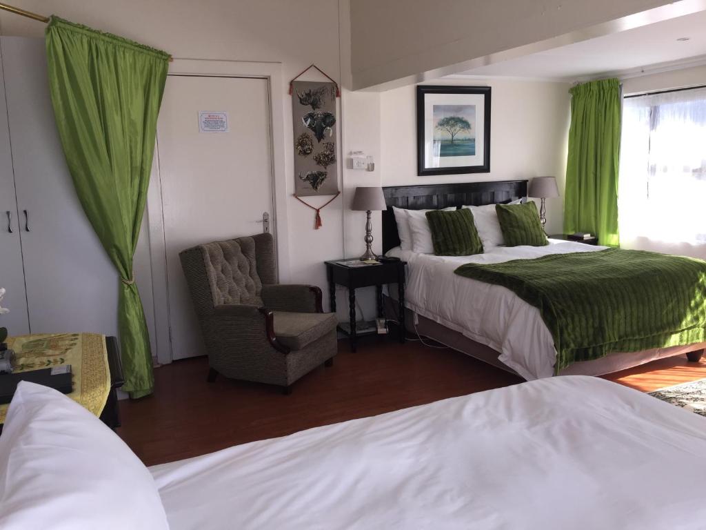 1 dormitorio con cama, silla y cortinas verdes en Ocean Dreams B&B, en Gonubie