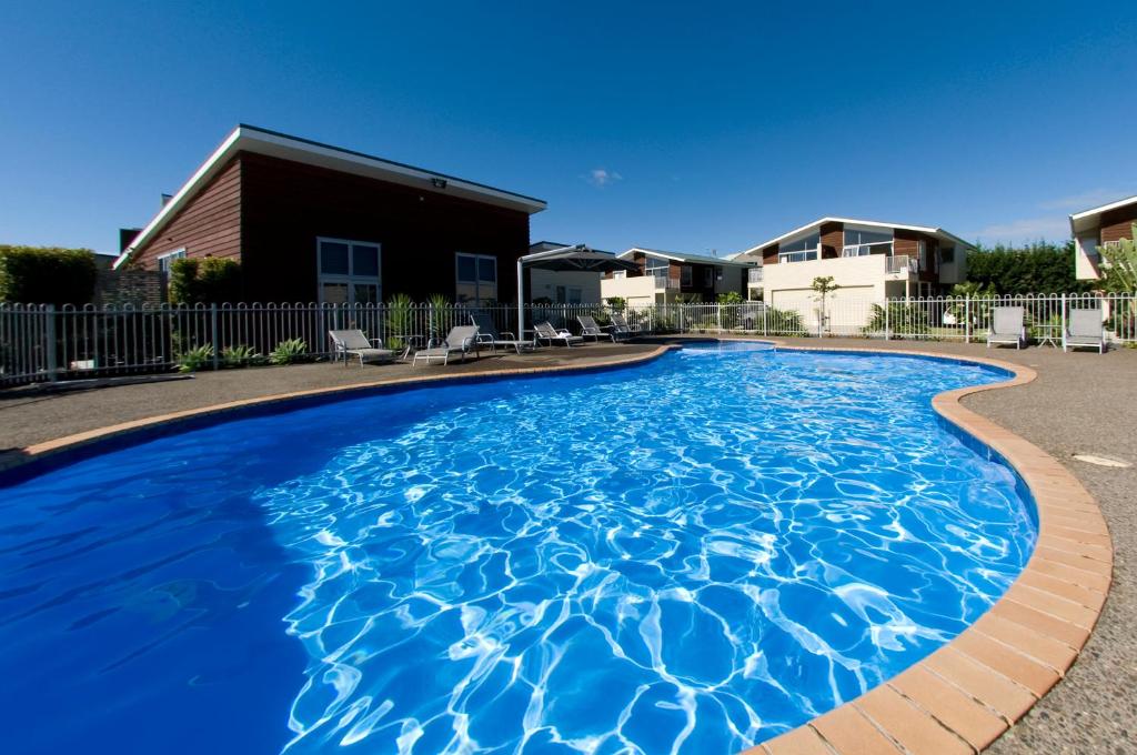 a swimming pool with blue water in front of a house at Beachside Resort Motel Whitianga in Whitianga