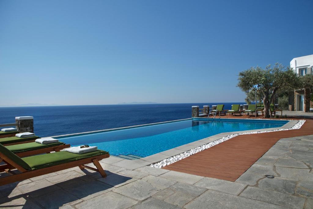 a swimming pool with chairs and the ocean in the background at Selana Suites in Chrisopigi
