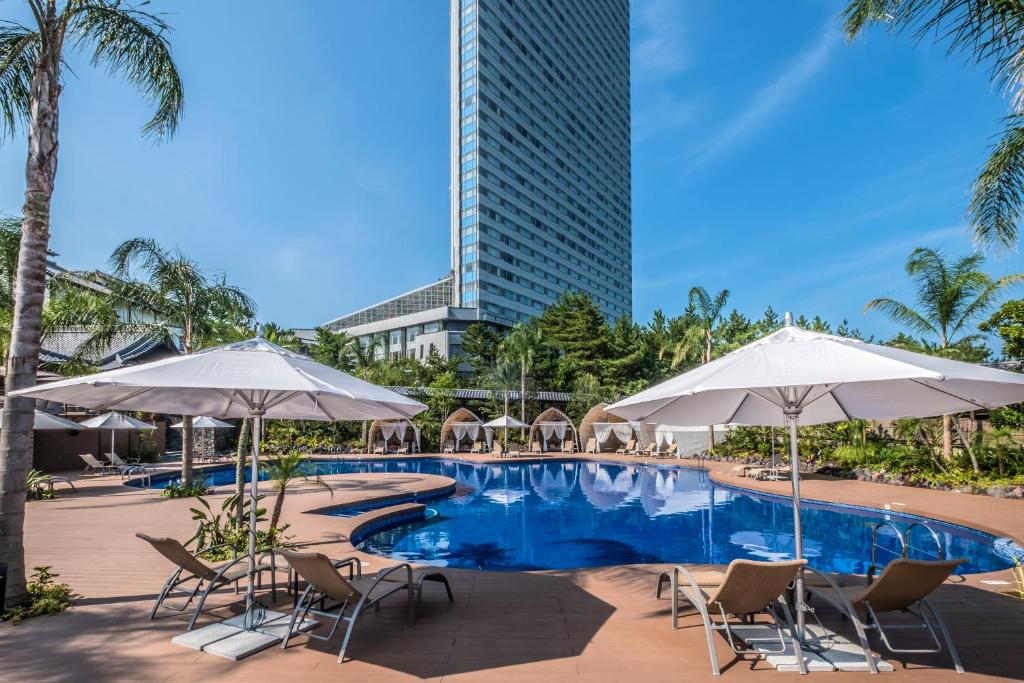 een zwembad met stoelen en parasols en een hoog gebouw bij Sheraton Grande Ocean Resort in Miyazaki