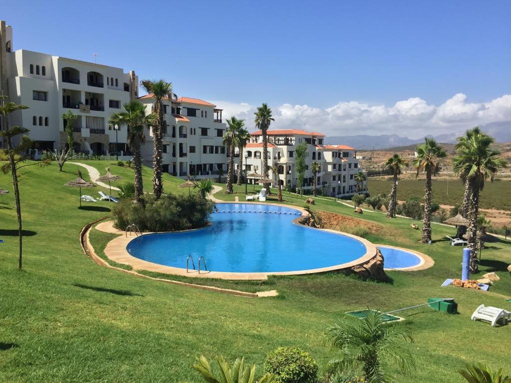 une grande piscine au milieu d'une pelouse avec des maisons dans l'établissement Lilac's Garden vue piscine, à M'diq