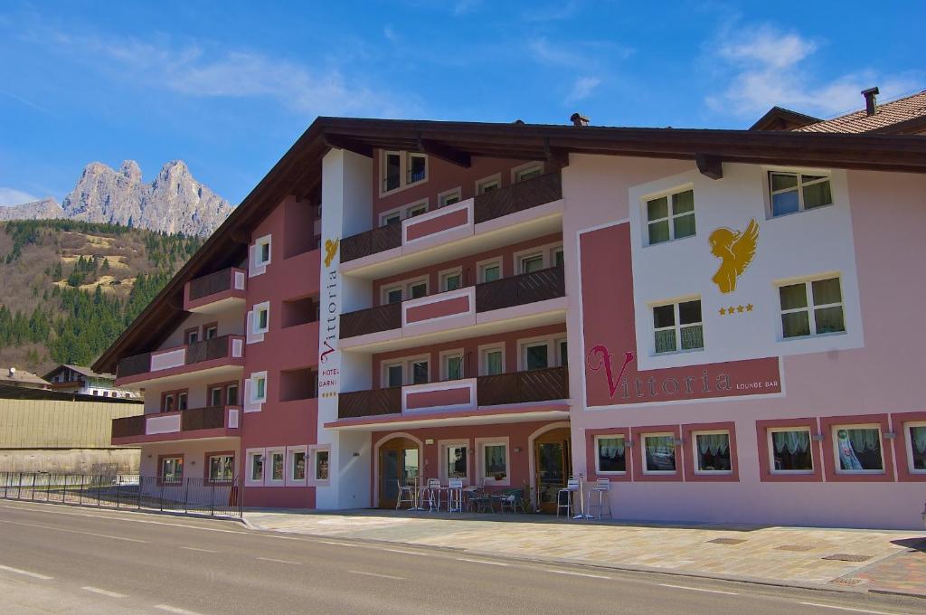 un gran edificio rosa con montañas en el fondo en Hotel Garni Vittoria en Fiera di Primiero
