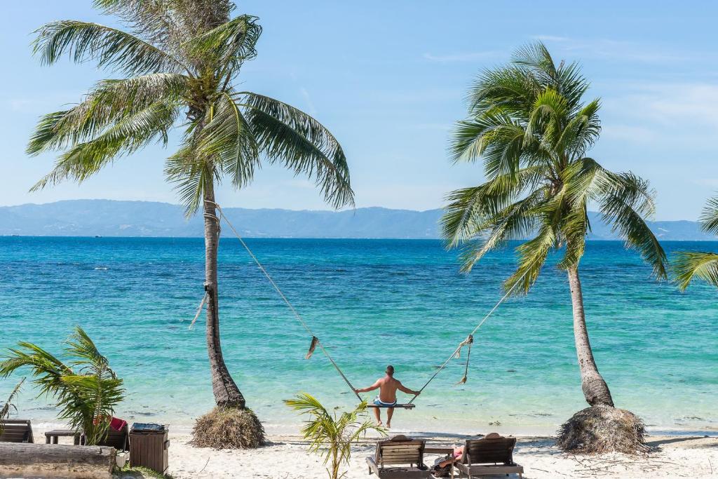 a man on a swing on a beach with two palm trees at Cocohut Beach Resort & Spa in Haad Rin