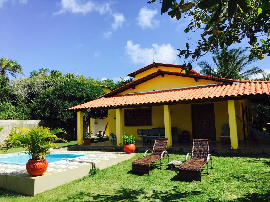 Ponta da Tulha的住宿－Casa Amarela na praia 14 pessoas，庭院内带游泳池和椅子的房子
