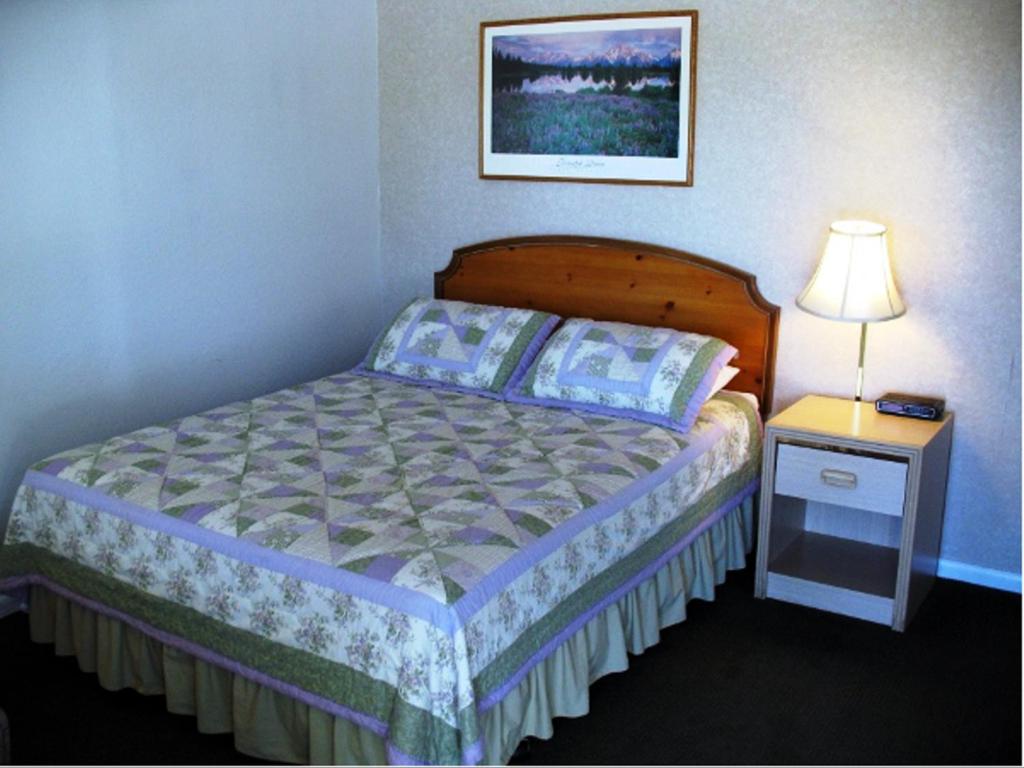 クラマスフォールズにあるゴールデン ウエスト モーテルのベッドルーム1室(ベッド1台、ナイトスタンド、ランプ付)