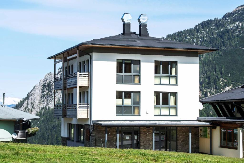 un edificio blanco en una colina con montañas al fondo en Alpenrose Nassfeld en Sonnenalpe Nassfeld