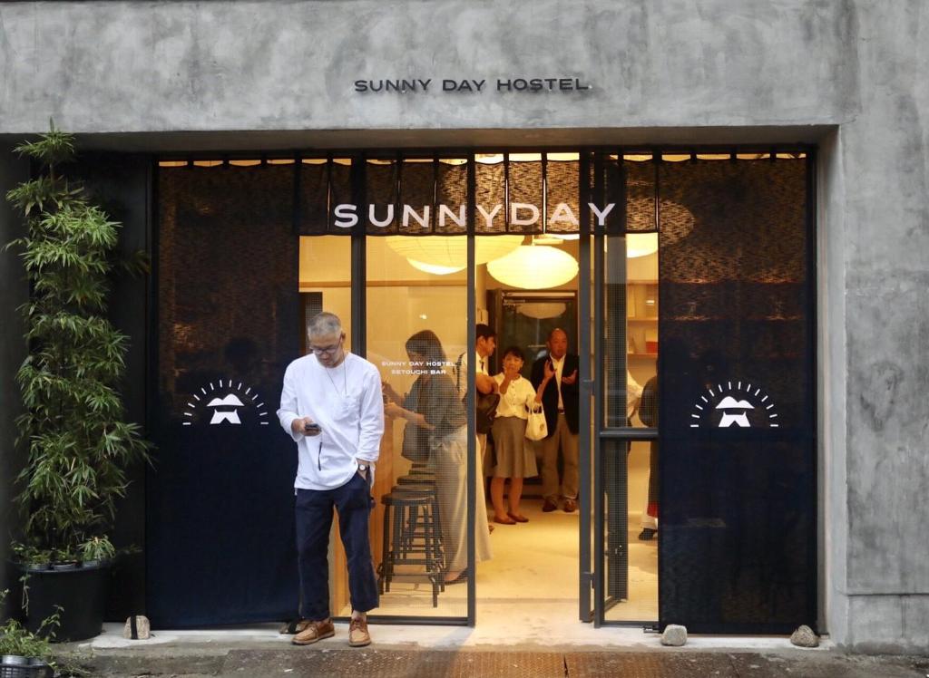 un hombre mirando su celular delante de una tienda en Sunny Day Hostel, en Takamatsu