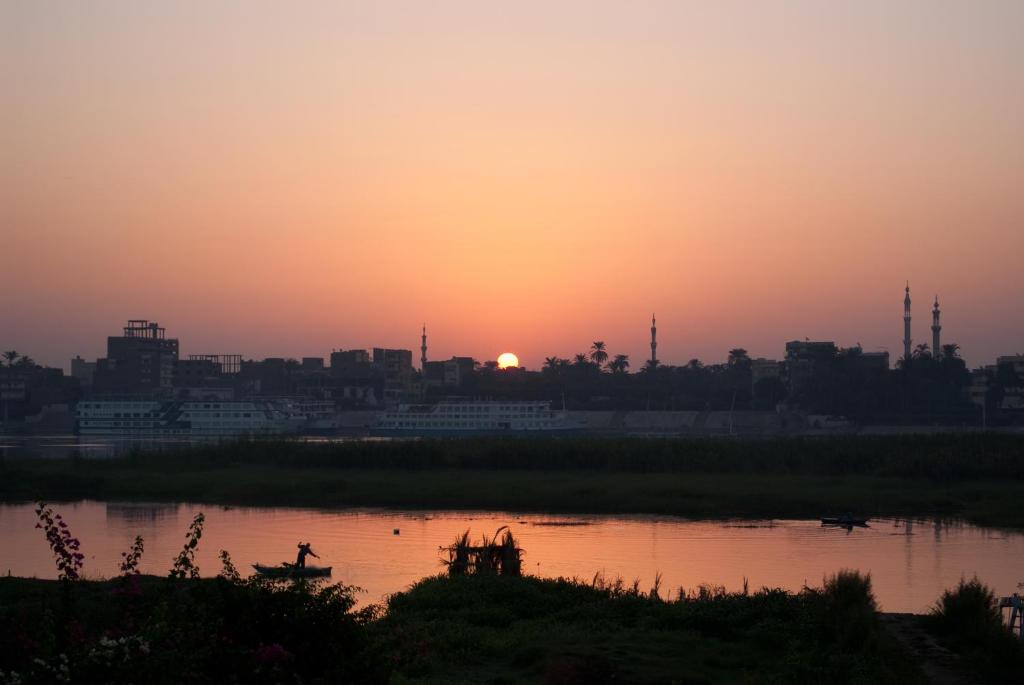 una puesta de sol sobre un río con una ciudad en el fondo en Al Baeirat Hotel, en Luxor