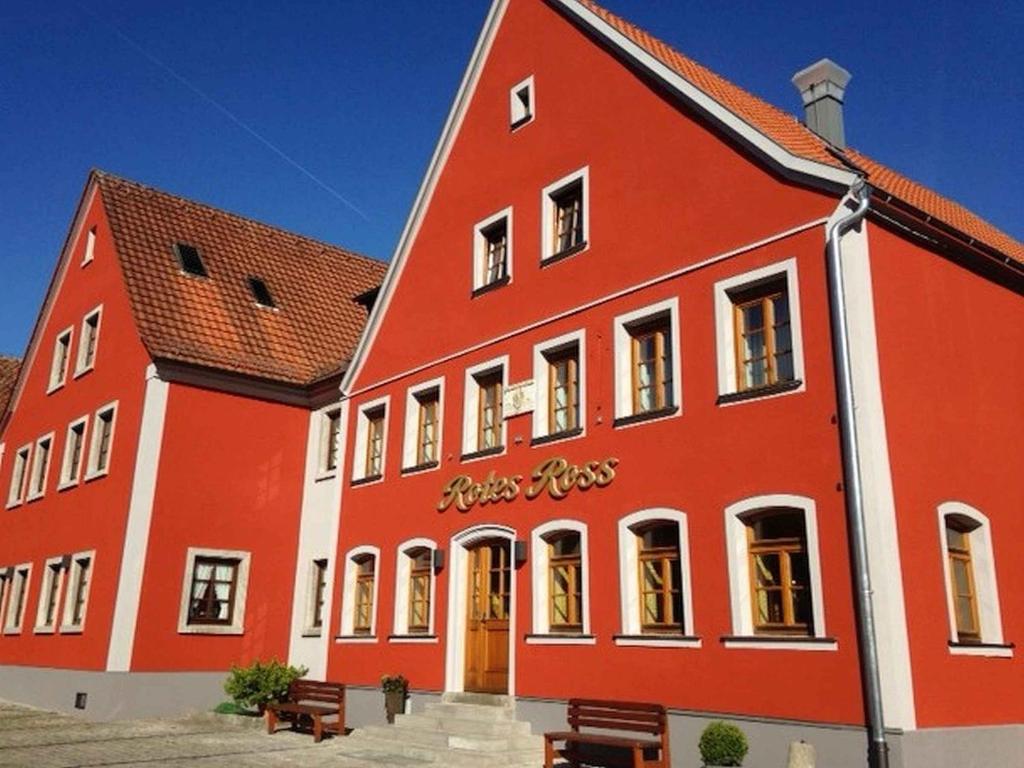 un grand bâtiment rouge avec des bancs devant lui dans l'établissement Hotel-Gasthof Rotes Roß, à Markt Einersheim