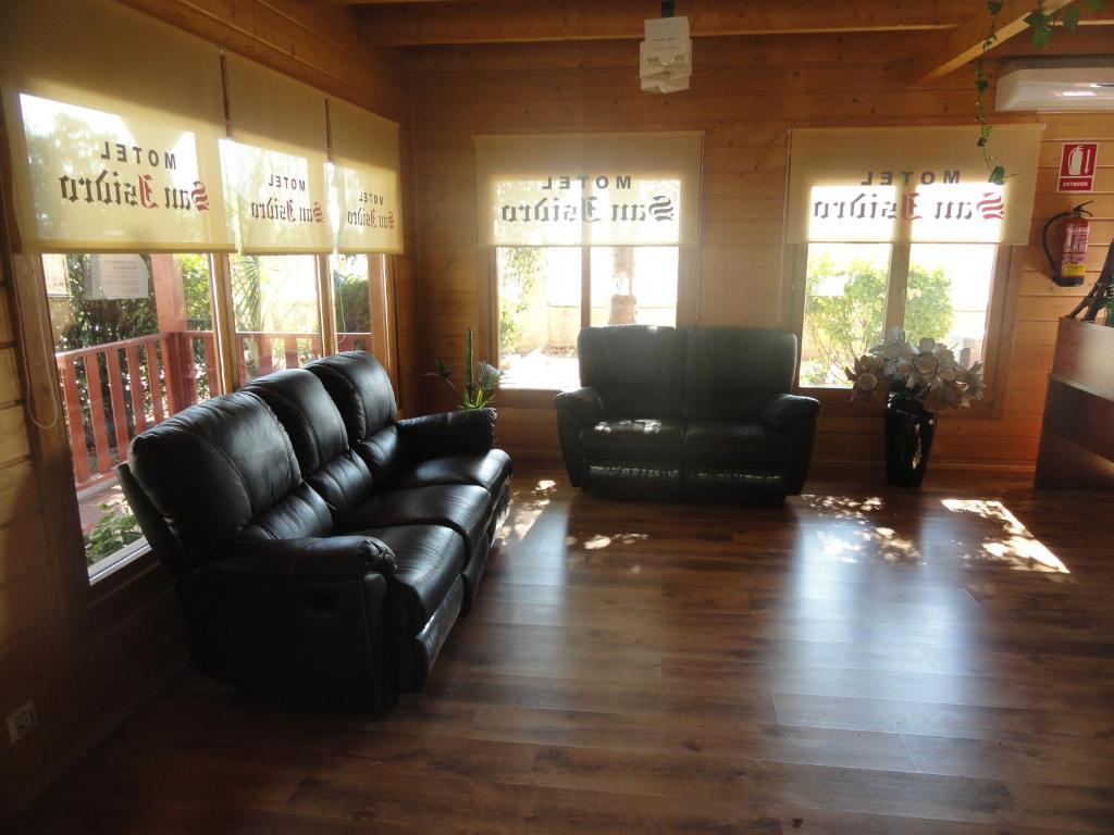 una sala de estar con 2 sofás de cuero negro y ventanas en Motel San Isidro en Villarrubio