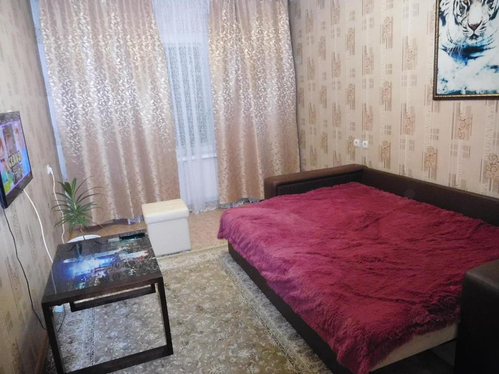 イジェフスクにあるАпартСтандарт Столичныйのベッドルーム(赤いベッド1台、テーブル付)