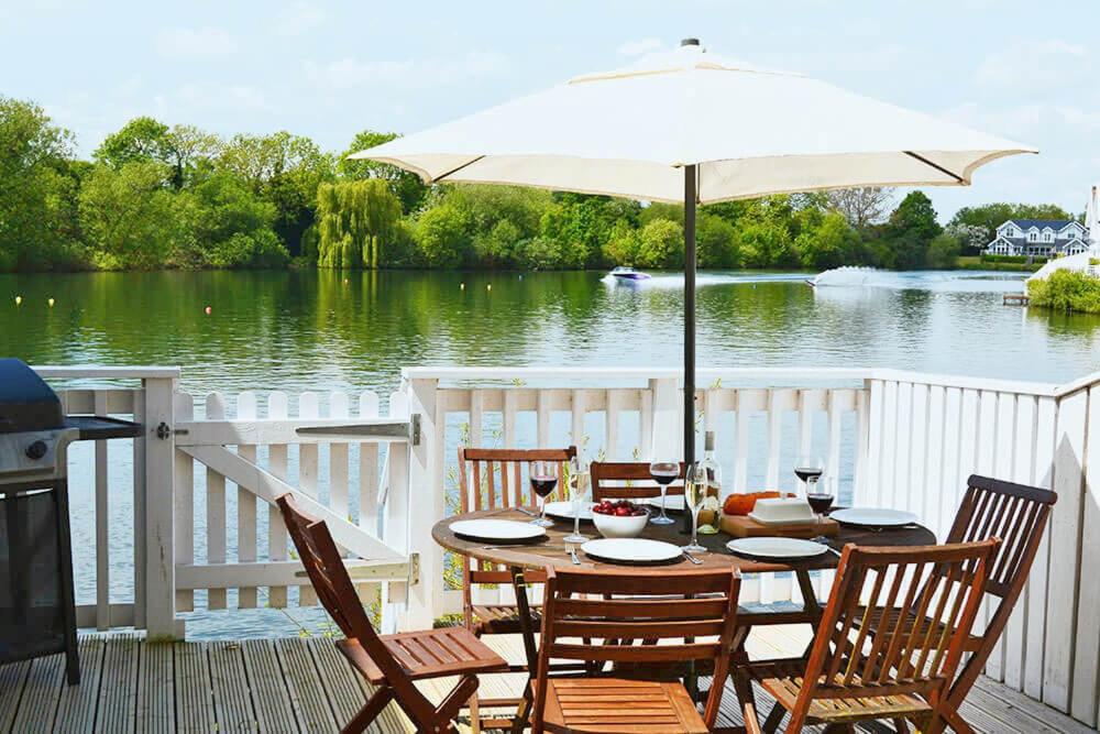 a table with an umbrella on a deck next to a lake at Swan Lake Lodge in Cirencester