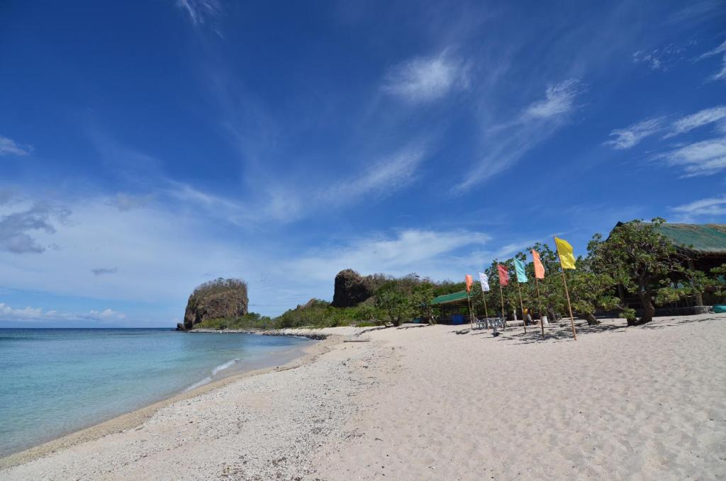 a beach with umbrellas and the ocean with rocks in the background at Eagle Point Beach and Dive Resort in Mabini