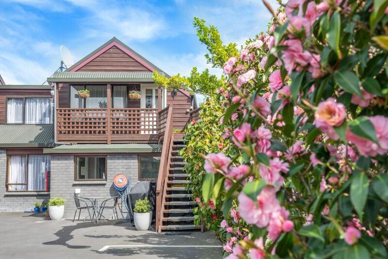 a house with a deck and some pink flowers at Strathern Motor Lodge in Christchurch